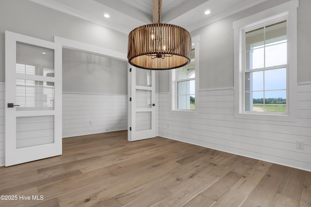 unfurnished dining area featuring hardwood / wood-style floors, a notable chandelier, beam ceiling, and wood walls