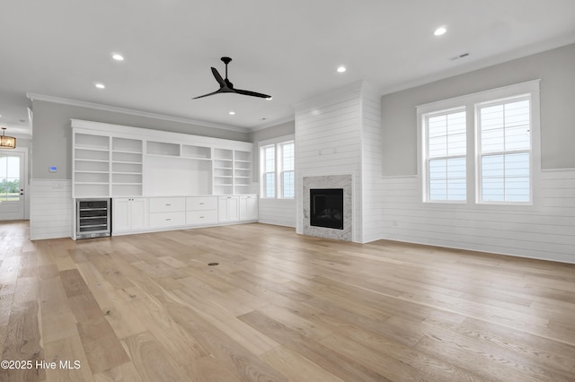 unfurnished living room with wine cooler, ornamental molding, light hardwood / wood-style floors, and a premium fireplace