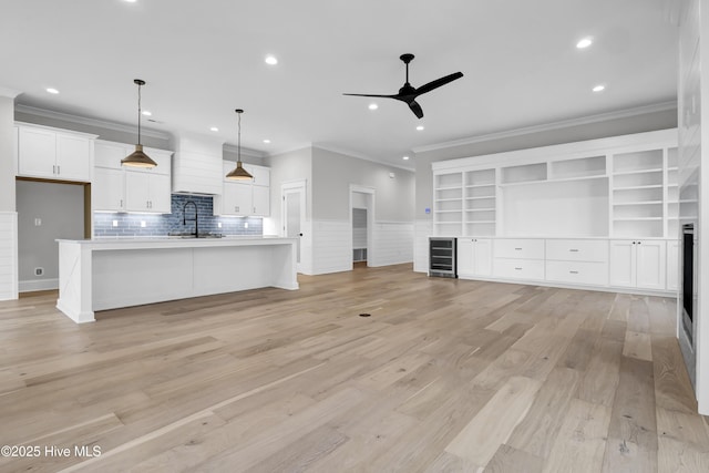 unfurnished living room featuring wine cooler, sink, crown molding, light hardwood / wood-style flooring, and ceiling fan