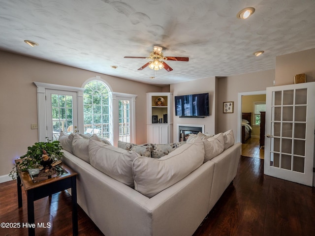 living room with dark wood-type flooring, ceiling fan, and a textured ceiling