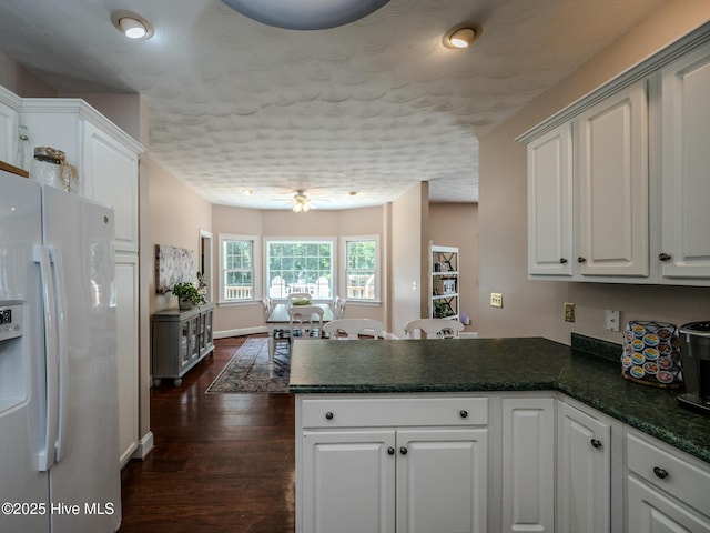 kitchen featuring ceiling fan, white refrigerator with ice dispenser, white cabinets, dark hardwood / wood-style flooring, and kitchen peninsula