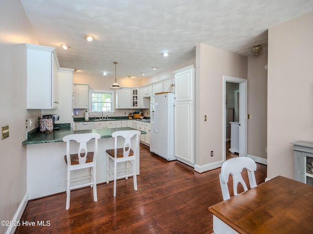 kitchen featuring dark wood-type flooring, sink, hanging light fixtures, white appliances, and white cabinets