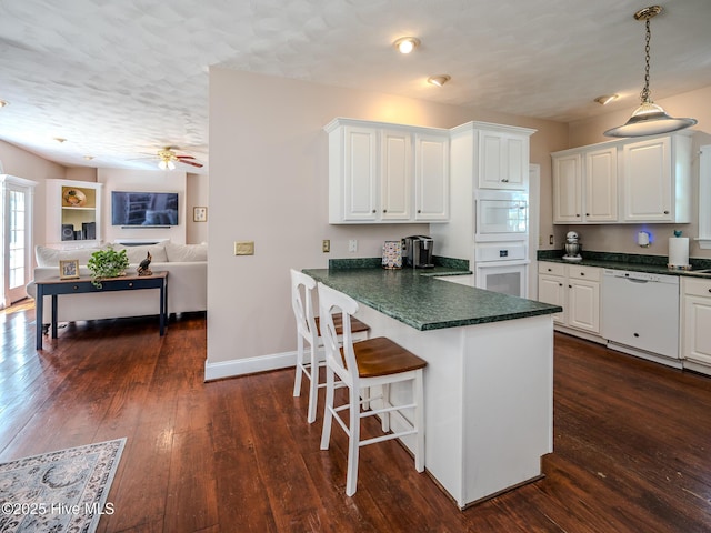 kitchen with white appliances, a breakfast bar area, white cabinetry, dark hardwood / wood-style flooring, and decorative light fixtures