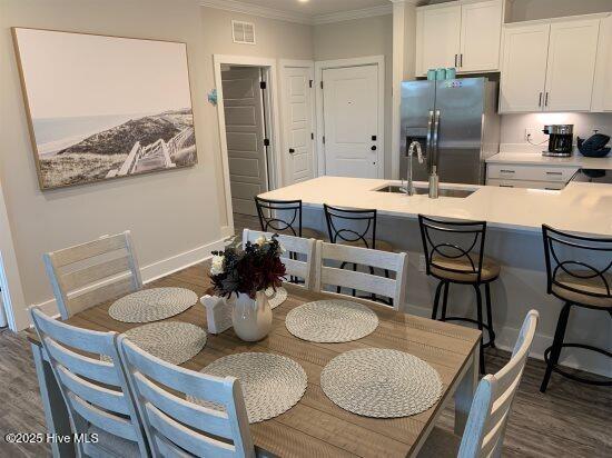 dining area with dark wood-type flooring, crown molding, and sink