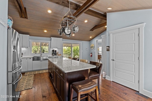 kitchen with a kitchen bar, sink, vaulted ceiling with beams, stainless steel fridge with ice dispenser, and a kitchen island