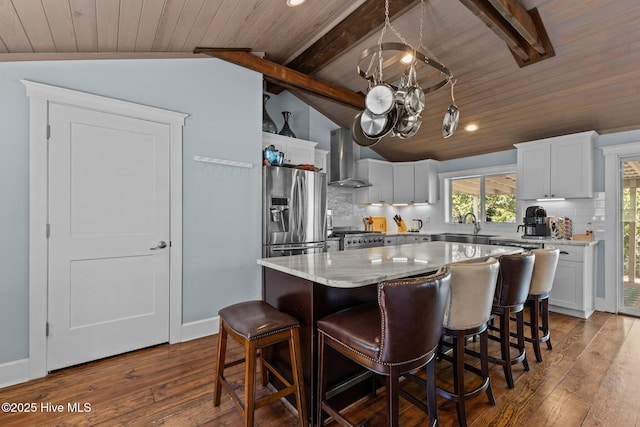 kitchen with stainless steel refrigerator with ice dispenser, sink, a center island, white cabinets, and wall chimney range hood