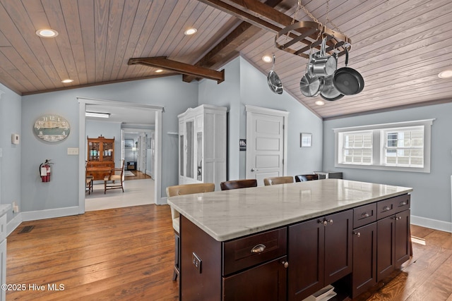 kitchen featuring vaulted ceiling with beams, a breakfast bar area, a center island, light stone counters, and dark wood-type flooring