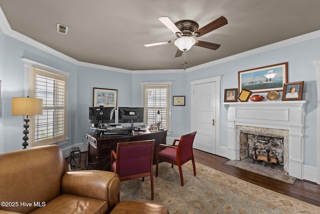 office featuring dark wood-type flooring, ceiling fan, ornamental molding, and a fireplace