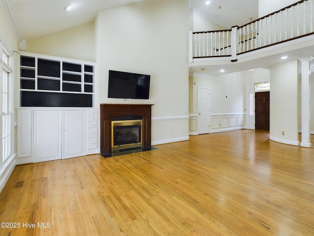 unfurnished living room with crown molding, high vaulted ceiling, light hardwood / wood-style floors, and ornate columns