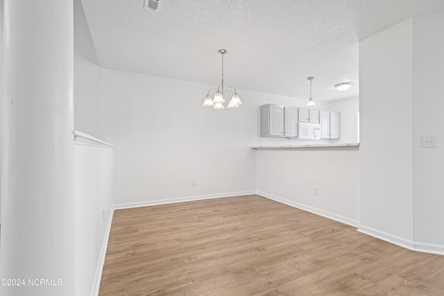 unfurnished room featuring a notable chandelier, a textured ceiling, and light wood-type flooring