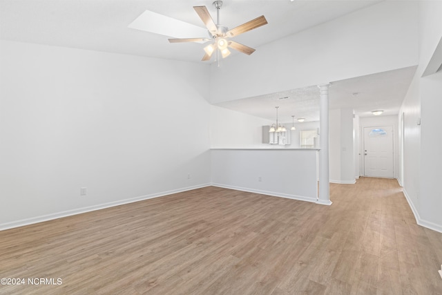 unfurnished living room with ceiling fan with notable chandelier, ornate columns, and light wood-type flooring