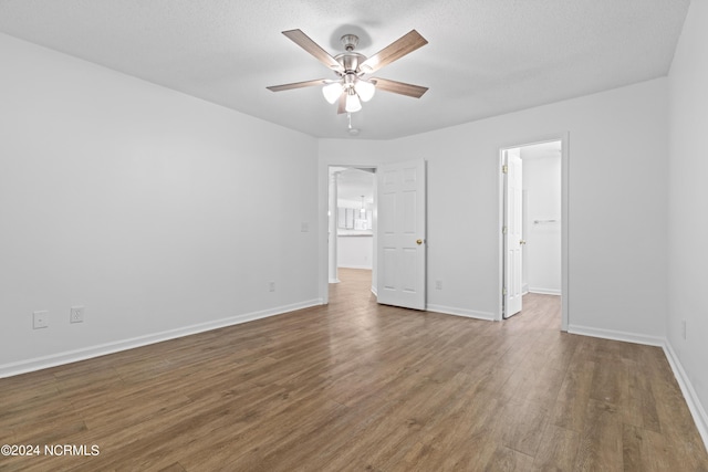 unfurnished bedroom featuring ceiling fan, a spacious closet, dark wood-type flooring, and a textured ceiling