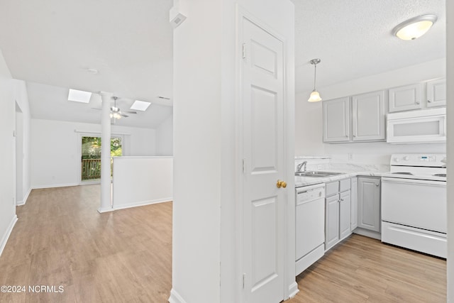 kitchen featuring sink, white appliances, light hardwood / wood-style flooring, hanging light fixtures, and a skylight