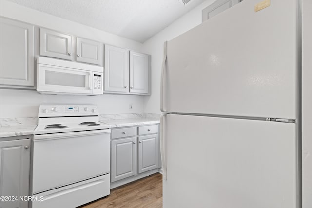 kitchen with light stone counters, white appliances, a textured ceiling, and light wood-type flooring