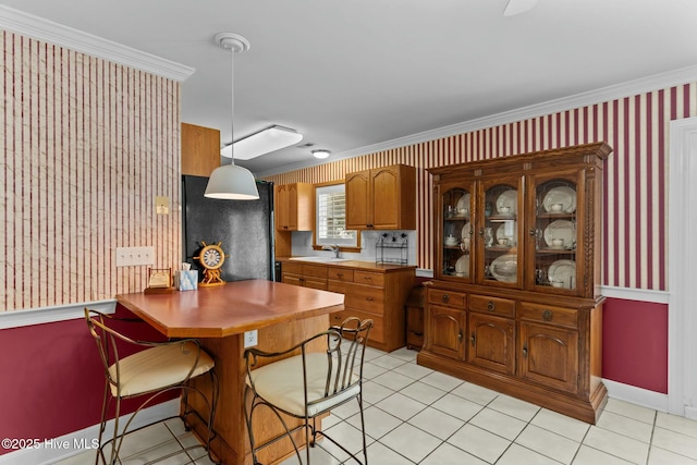 kitchen featuring light tile patterned flooring, sink, hanging light fixtures, crown molding, and black fridge