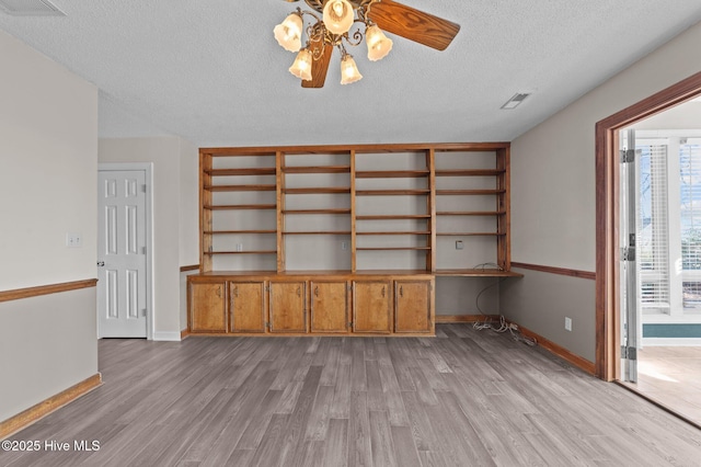 unfurnished living room with ceiling fan, built in desk, light hardwood / wood-style floors, and a textured ceiling