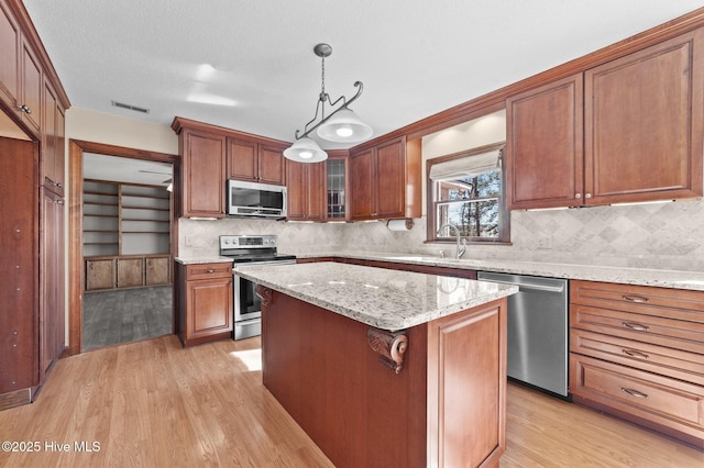 kitchen featuring light hardwood / wood-style flooring, appliances with stainless steel finishes, light stone countertops, a kitchen island, and decorative light fixtures