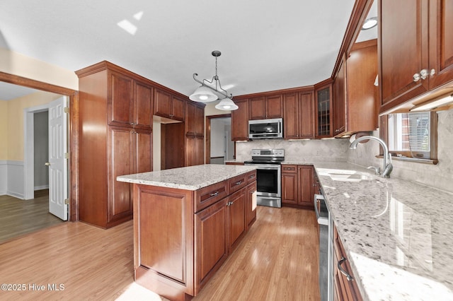 kitchen featuring pendant lighting, appliances with stainless steel finishes, a center island, light stone counters, and light wood-type flooring