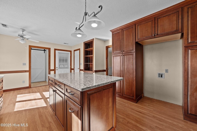 kitchen with light hardwood / wood-style floors, light stone countertops, a kitchen island, decorative light fixtures, and a barn door