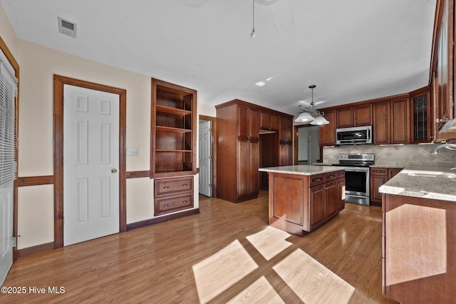 kitchen featuring sink, light hardwood / wood-style flooring, appliances with stainless steel finishes, a center island, and decorative light fixtures