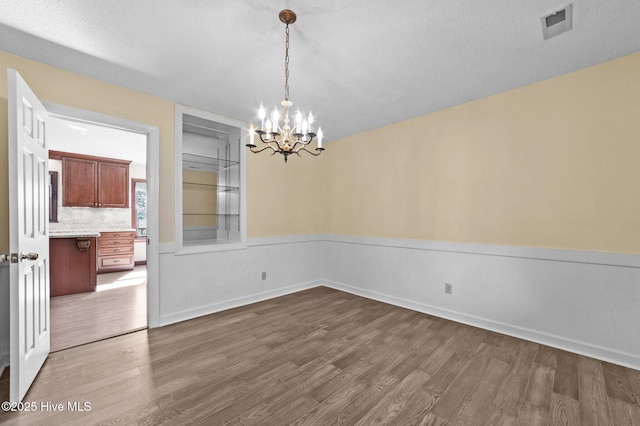 unfurnished dining area with an inviting chandelier, dark hardwood / wood-style floors, and a textured ceiling