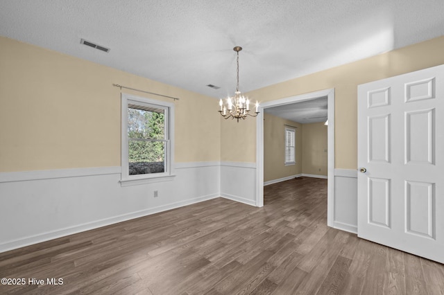 unfurnished dining area with hardwood / wood-style flooring, a textured ceiling, and a notable chandelier