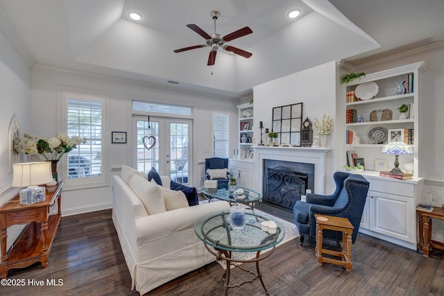 living room with french doors, dark wood-type flooring, ornamental molding, a tray ceiling, and built in features