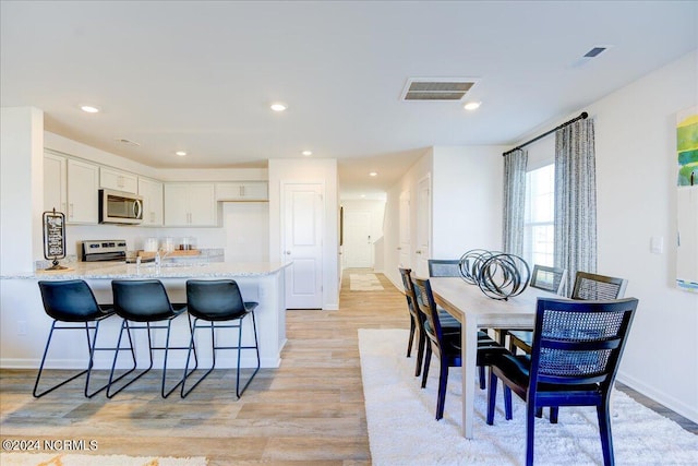 kitchen featuring appliances with stainless steel finishes, white cabinetry, kitchen peninsula, light stone countertops, and light wood-type flooring