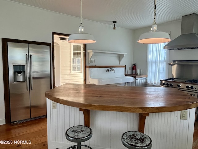 kitchen with butcher block countertops, sink, hardwood / wood-style flooring, stainless steel appliances, and exhaust hood