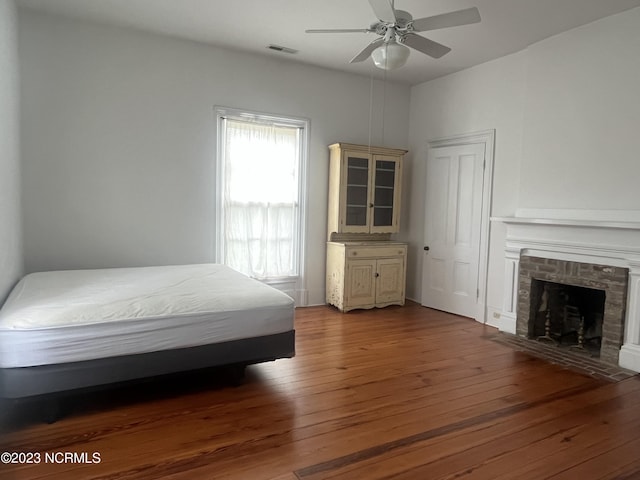 bedroom with dark hardwood / wood-style flooring, a brick fireplace, and ceiling fan