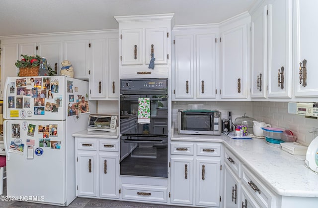 kitchen featuring double oven, white cabinetry, decorative backsplash, white fridge, and light stone countertops