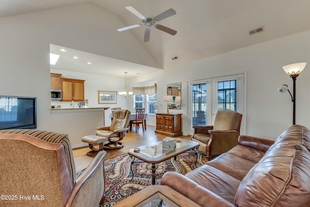 living room featuring french doors, ceiling fan with notable chandelier, high vaulted ceiling, and light hardwood / wood-style flooring