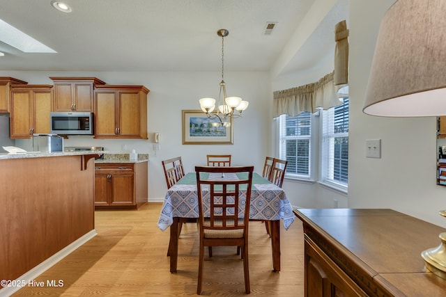 dining space featuring a notable chandelier, a skylight, and light hardwood / wood-style floors