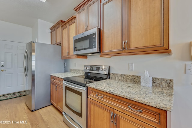 kitchen with light stone countertops, light hardwood / wood-style floors, and appliances with stainless steel finishes