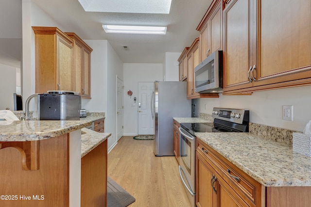 kitchen with light stone counters, a skylight, light hardwood / wood-style flooring, appliances with stainless steel finishes, and a kitchen breakfast bar