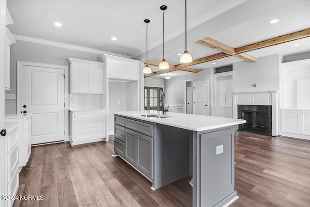 kitchen with sink, dark wood-type flooring, white cabinetry, hanging light fixtures, and a center island with sink