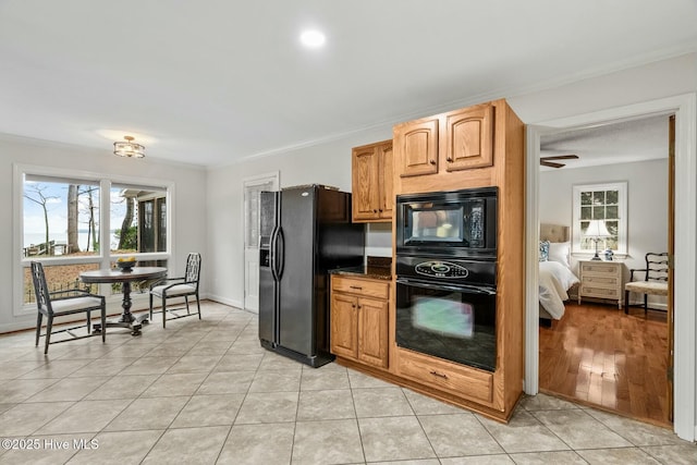 kitchen with ornamental molding, light tile patterned floors, dark stone counters, and black appliances