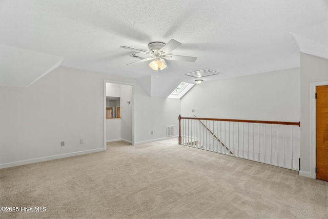 additional living space with lofted ceiling with skylight, light carpet, ceiling fan, and a textured ceiling