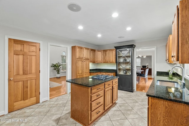 kitchen featuring sink, light tile patterned floors, dark stone countertops, ornamental molding, and a kitchen island