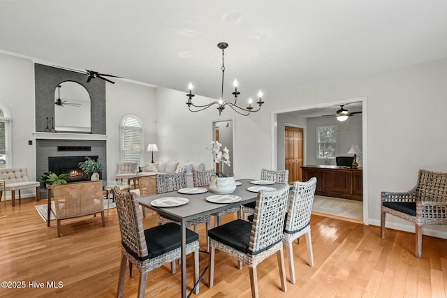 dining room with a fireplace, ceiling fan with notable chandelier, and light wood-type flooring