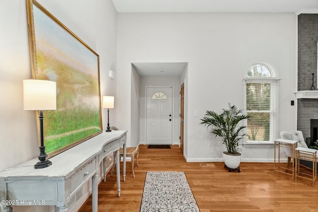 foyer entrance with a brick fireplace, wood-type flooring, and a high ceiling