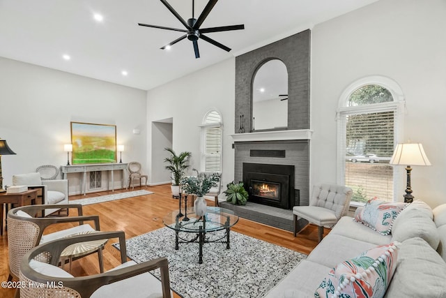 living room featuring hardwood / wood-style floors, a fireplace, ceiling fan, and a high ceiling