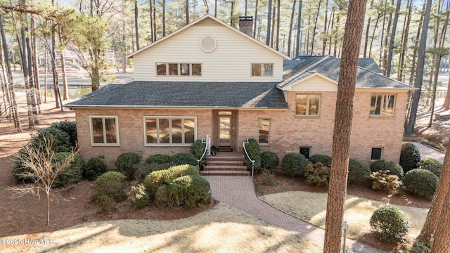 view of front facade with brick siding, crawl space, a chimney, and roof with shingles