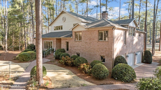 view of front of home featuring a garage, brick siding, roof with shingles, and a chimney