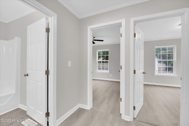 corridor with light wood finished floors, ornamental molding, and baseboards