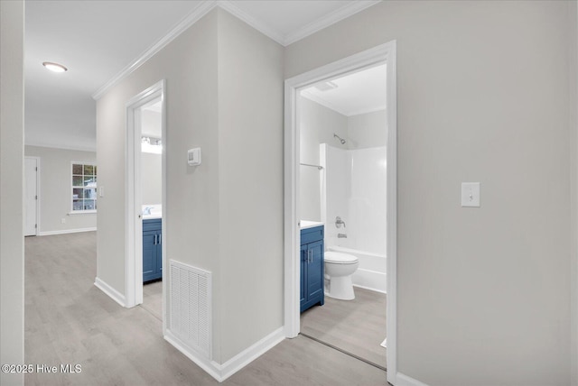 corridor with light wood-style floors, baseboards, visible vents, and crown molding