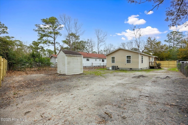 back of property with cooling unit, a storage shed, an outdoor structure, fence, and crawl space