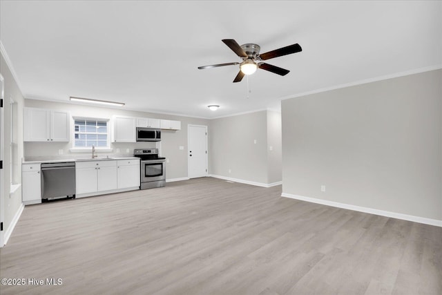 kitchen with stainless steel appliances, a sink, white cabinets, open floor plan, and light countertops