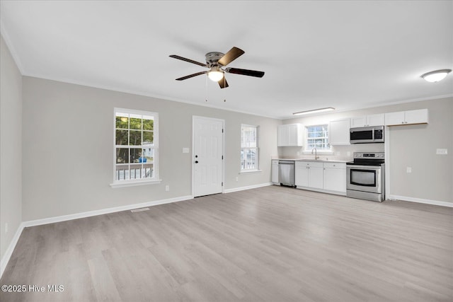 kitchen featuring light countertops, appliances with stainless steel finishes, open floor plan, white cabinetry, and a sink