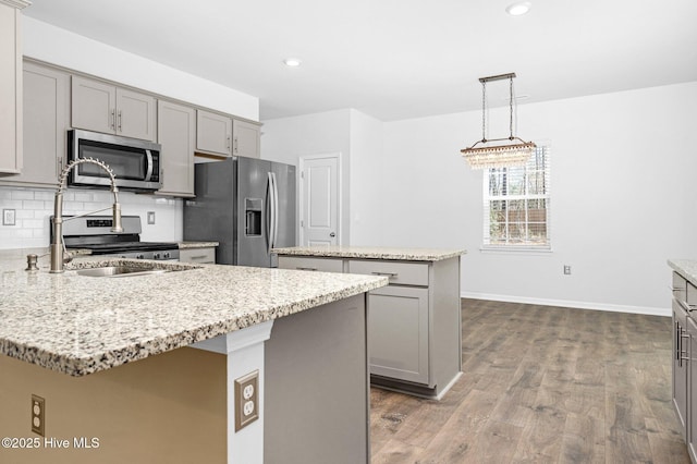 kitchen featuring backsplash, gray cabinetry, appliances with stainless steel finishes, wood finished floors, and a peninsula